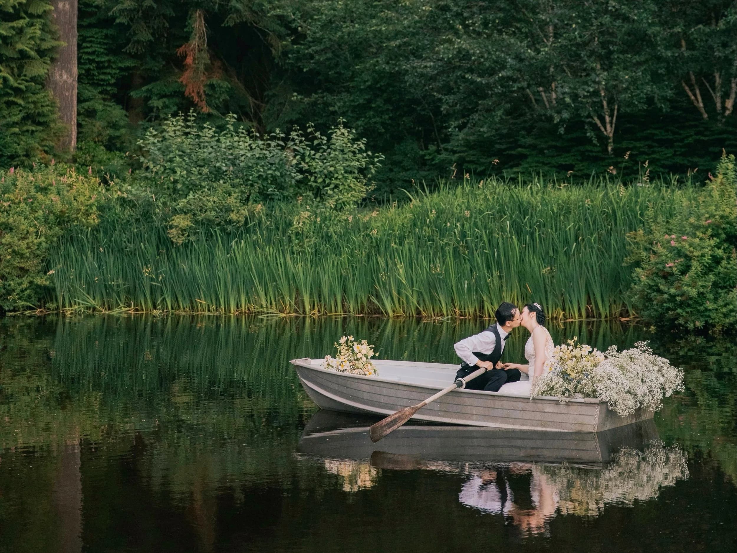 A couple in a rowboat on the still iris-ringed pond, the forest reflected in the water
