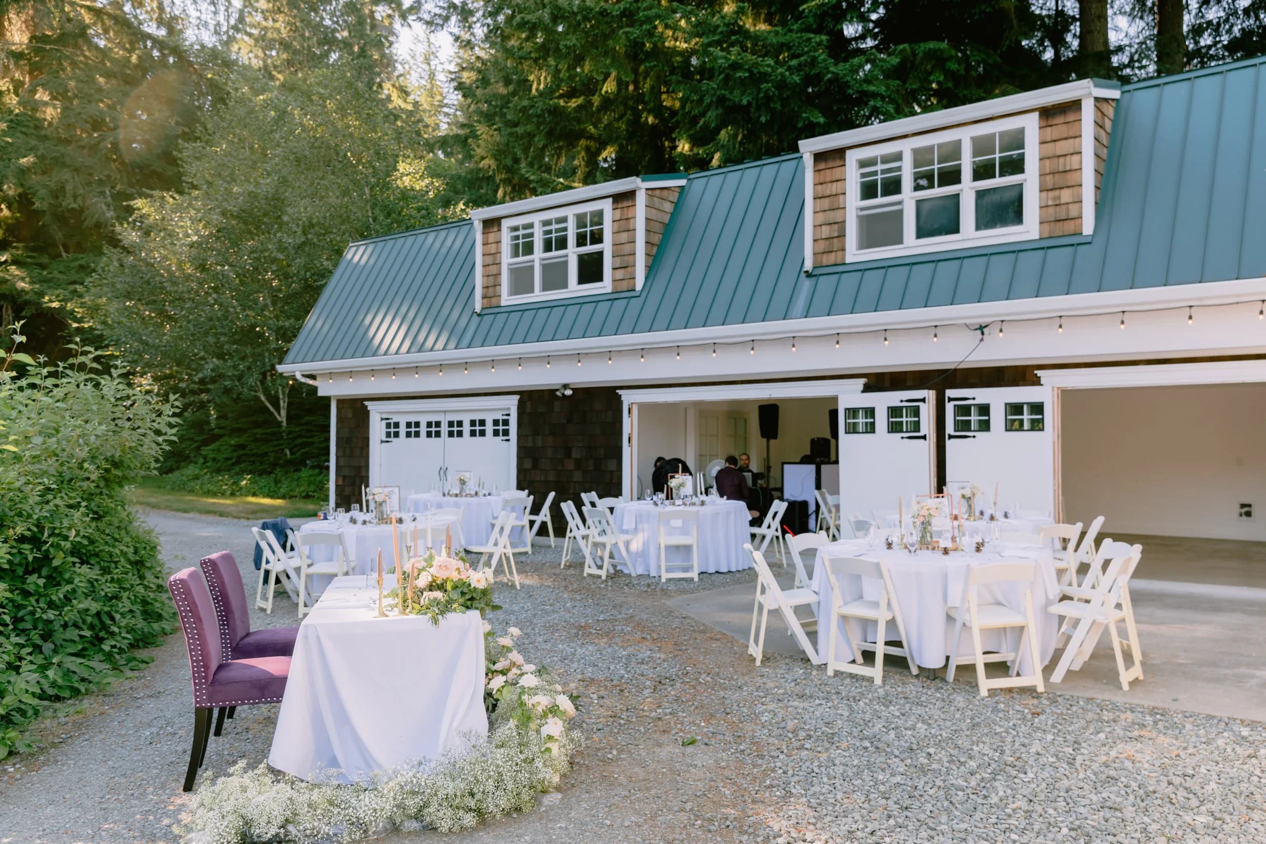 The two-story Carriage House with its teal gambrel roof, set with round reception tables on the gravel courtyard